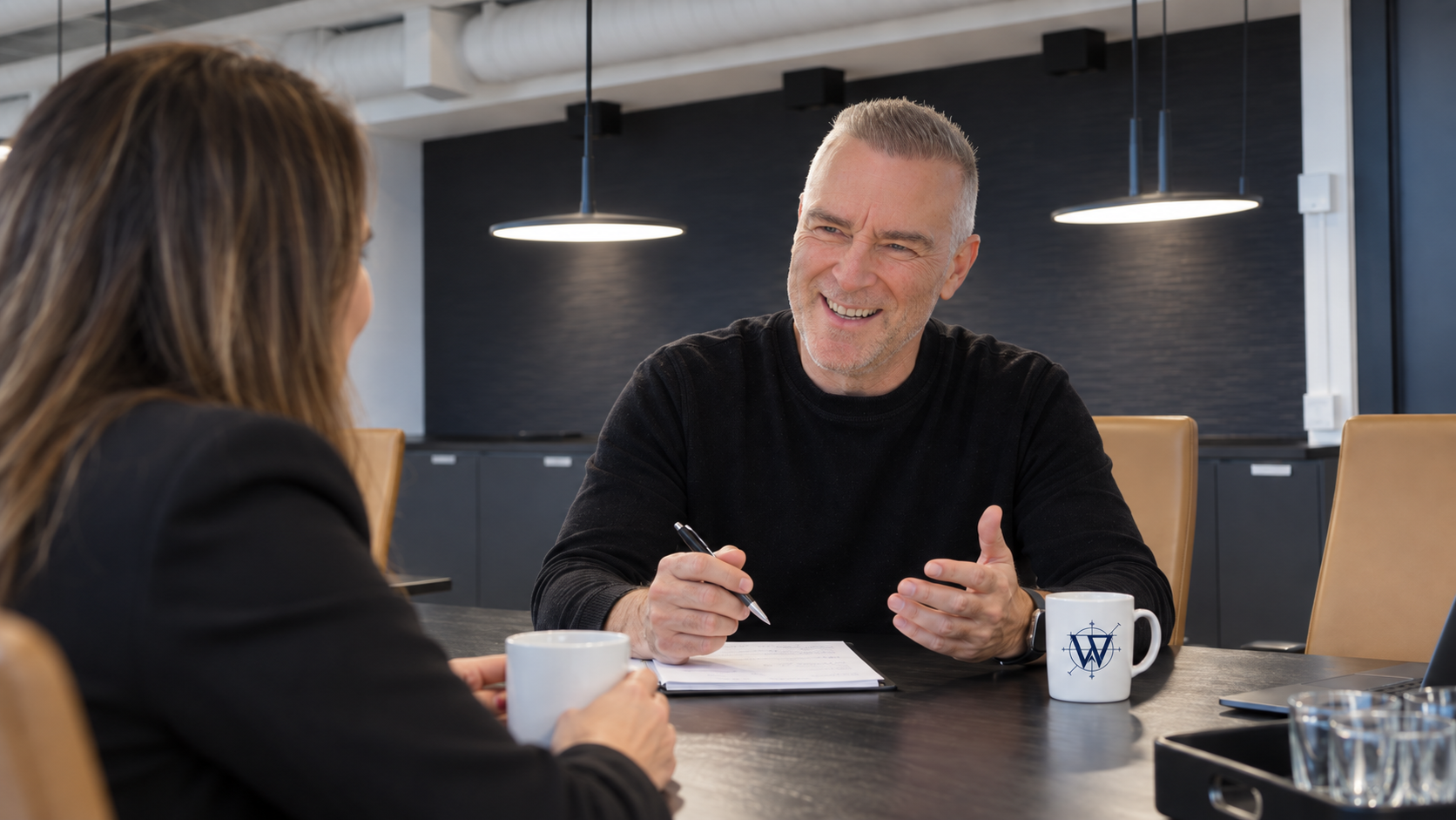 Two colleagues discuss documents at a conference table in a modern office.